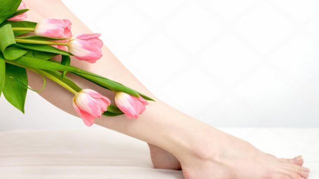 Smooth, well-cared-for legs and feet resting beside a bouquet of pink tulips after a pedicure