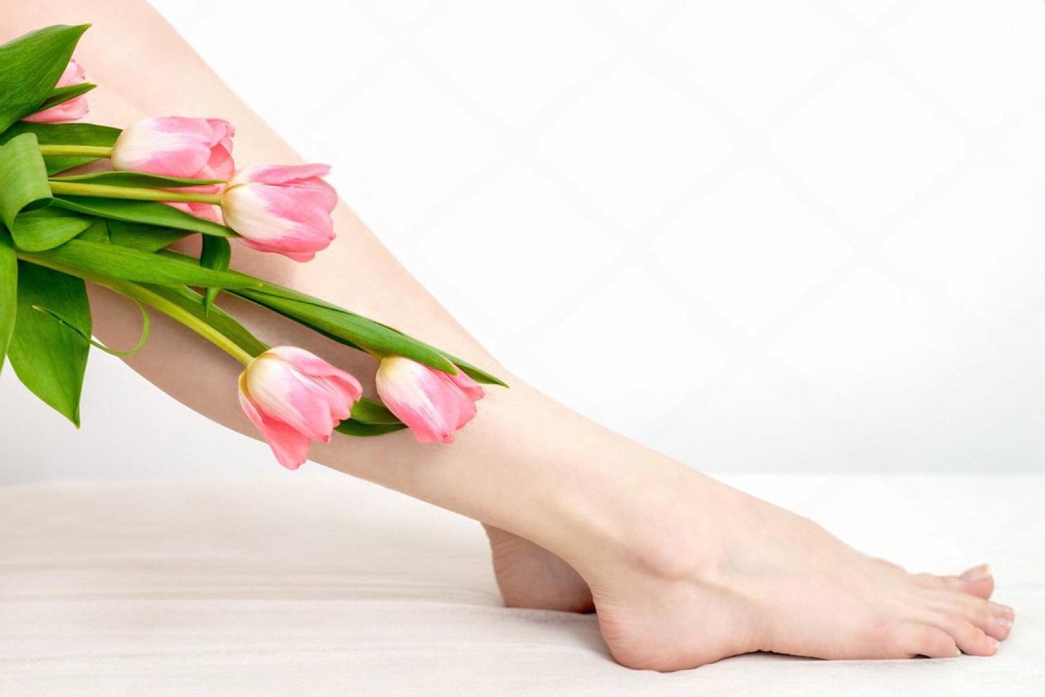 Smooth, well-cared-for legs and feet resting beside a bouquet of pink tulips after a pedicure