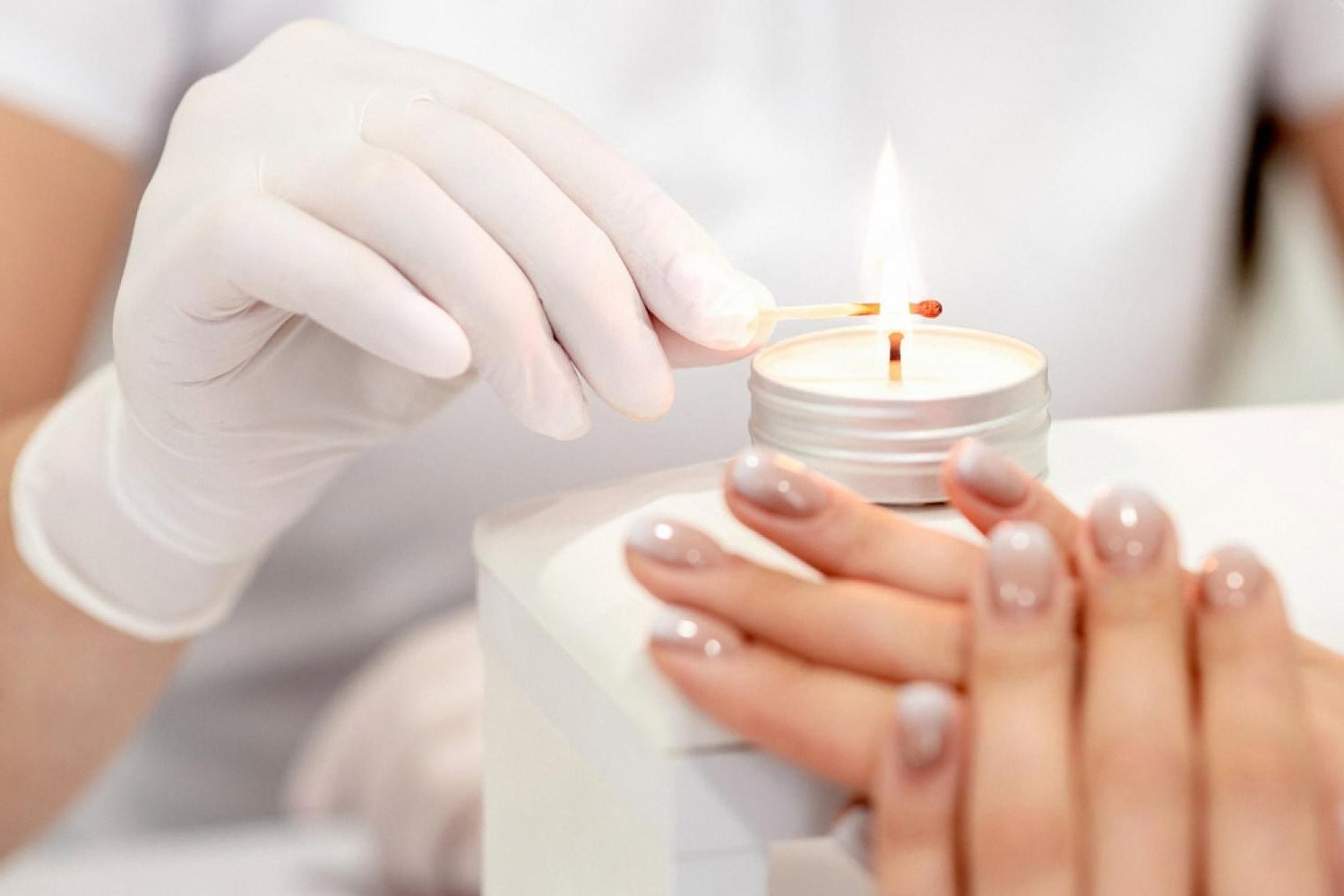 Technician in white gloves performing a paraffin manicure on freshly polished nails at a Dubai salon