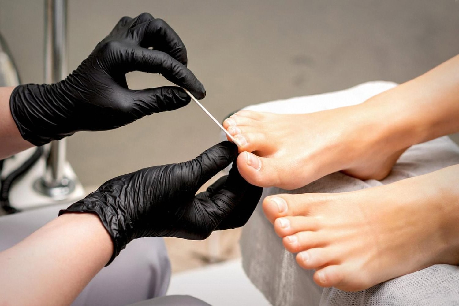 Pedicurist in black gloves filing a client's toenail during a professional pedicure treatment